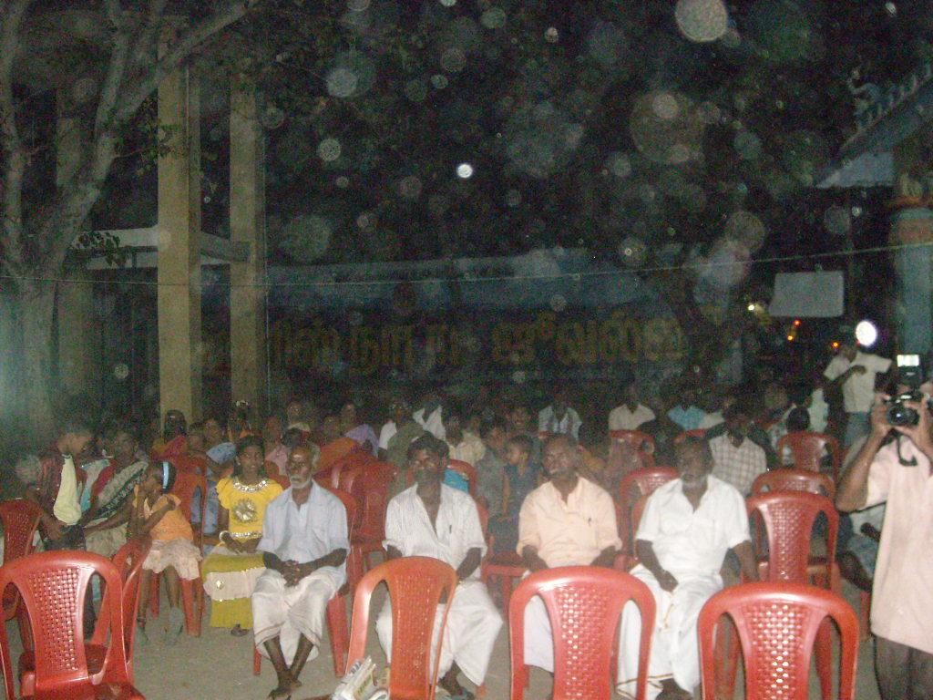 Large community meeting with farmers seated under trees